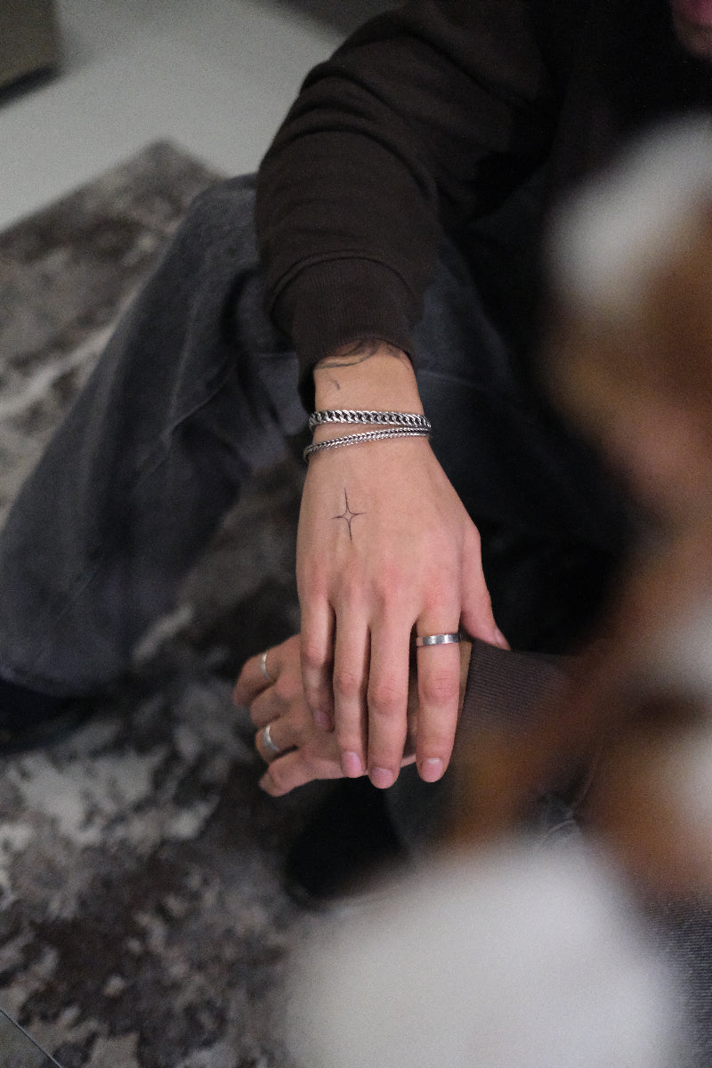 Een zittende man die met zijn ellenbogen op zijn knieën rust. Hij heeft zijn handen over elkaar en op de bovenzijde van zijn hand, ter hoogte van zijn ringvinger draagt hij het ontwerp van een minimalistische vierpuntige ster.